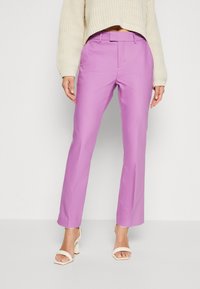 Pantalon lilas avec une coupe droite, présentant une texture lisse, des passants de ceinture et une taille mi-haute, associé à un pull court crème et des talons.