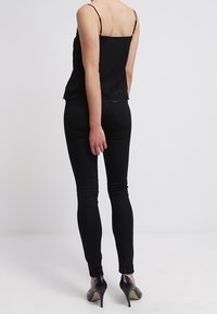 Černý top s krajkovým lemem, nastavitelnými ramínky a přiléhavým střihem, kombinovaný s černými vysokými skinny džíny a černými podpatky.