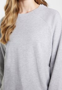 Sudadera gris con un acabado texturizado, mangas raglán y cuello redondo, que cuenta con un corte relajado y una tela suave.