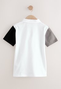 Póló fehér testtel, fekete bal ujjal és szürke jobb ujjal. Klasszikus gallérral és sima, finom szövésű anyaggal rendelkezik.