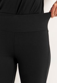 Schwarze Leggings mit einem breiten, bequemen Bund. Hergestellt aus einem glatten, dehnbaren Material, mit minimalen Nähten und einem taillierten Design.