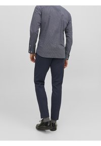 Granatowa teksturowana koszula w kratę, z mankietami na guziki i zaokrąglonym dołem, zestawiona z granatowymi spodniami i czarnymi butami. Jednolite tło.