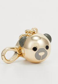 Porte-clés en forme d'ours de couleur or avec des yeux noirs, un museau gris et des oreilles vert foncé. Comprend un clip robuste pour attache.