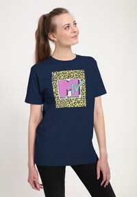 Camiseta azul marino con un gráfico cuadrado que presenta un logo de MTV en color rosa sobre un fondo de estampado de leopardo verde, fabricada en suave tela de algodón.