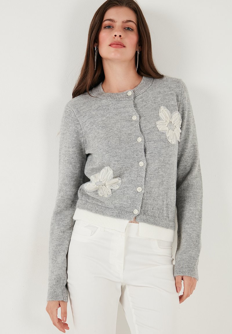 Cardigan gri din material moale, cu guler rotund, închidere cu nasturi și broderie florală albă pe șolduri. Accesorizat cu manșete dublate.
