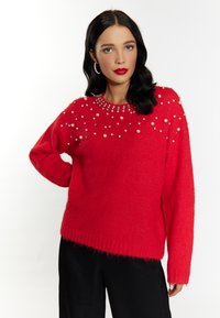 Maglione rosso a maglia con scollatura rotonda, decorazioni in perle e pietre brillanti sul petto, e polsini e orlo a coste.