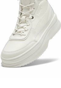 White high-top sneakers made of textured synthetic leather, featuring lace-up design, rubber sole with ridges, and subtle branding accents.