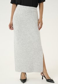 Jupe maxi en tricot gris avec une taille haute, fente latérale et texture douce, associée à des escarpins noirs à bout pointu avec un détail de boucle.