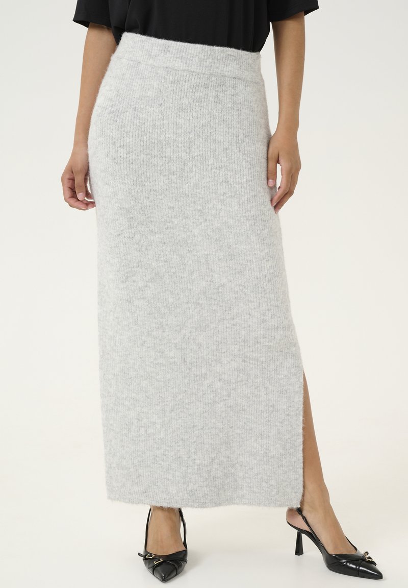 Gonna maxi grigia a maglia con vita alta, spacco laterale e texture morbida, abbinata a décolleté nere a punta con dettaglio a fibbia.