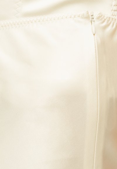 Κοντινή λήψη κρεμ σατέν υφάσματος με μικρό, μερικώς ανοιχτό πλαϊνό φερμουάρ και ραφές στην πάνω άκρη.