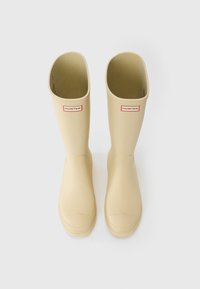 Beige rubber rain boots with a tall, straight shaft, rounded toes, and a HUNTER logo at the front. Smooth texture and simple design.