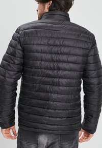 Chaqueta de plumas negra con costuras horizontales, cuello alto y una textura suave y brillante. Presenta puños elásticos y una silueta entallada.