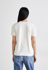 Krótki rękaw, kremowy t-shirt z okrągłym dekoltem, wykonany z miękkiej bawełny, w luźnym kroju, z gładkim tyłem bez widocznych wzorów.