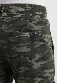 Shorts van camouflagepatroonstof in donkergroen en zwart, met een achterzakdetail, textuurafwerking en een aansluitende tailleband.