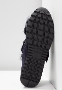 Black rubber sole with a textured grip, featuring a navy upper with soft fur accents and a strap for secure fastening.