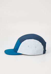 Caps med en turkise visir og marineblå og hvite paneler, laget av lett stoff. Har ventilasjonslufter og justerbar stropp.