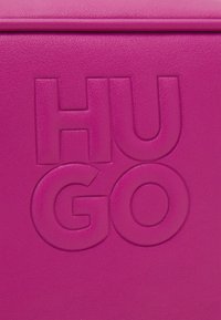 Fuchsiafarbenes Lederprodukt mit strukturiertem Muster und geprägt großem "HUGO"-Logo. Saubere Kanten und glatte Oberfläche mit modernem Design.