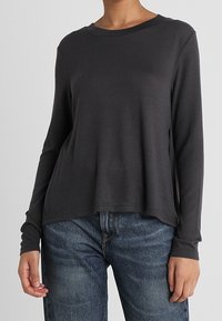 Maglietta a maniche lunghe color carbone in un materiale morbido e leggero, con scollatura arrotondata e vestibilità leggermente ampia. Abbinata a jeans blu.