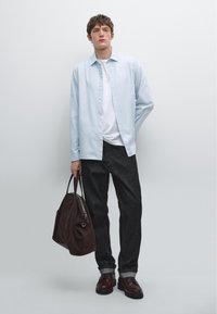 Camicia azzurra chiara, t-shirt bianca, jeans in denim scuro, borsa in suede marrone e scarpe bordeaux. Design semplice con vestibilità rilassata.