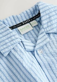 Col de chemise rayé texturé bleu clair avec étiquette "Baker by Ted Baker" et bouton blanc sur un fond clair.