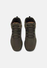 Zapatos de senderismo verde oliva con parte superior sintética, superficie texturizada, diseño con cordones, cuello acolchado y un interior naranja contrastante.