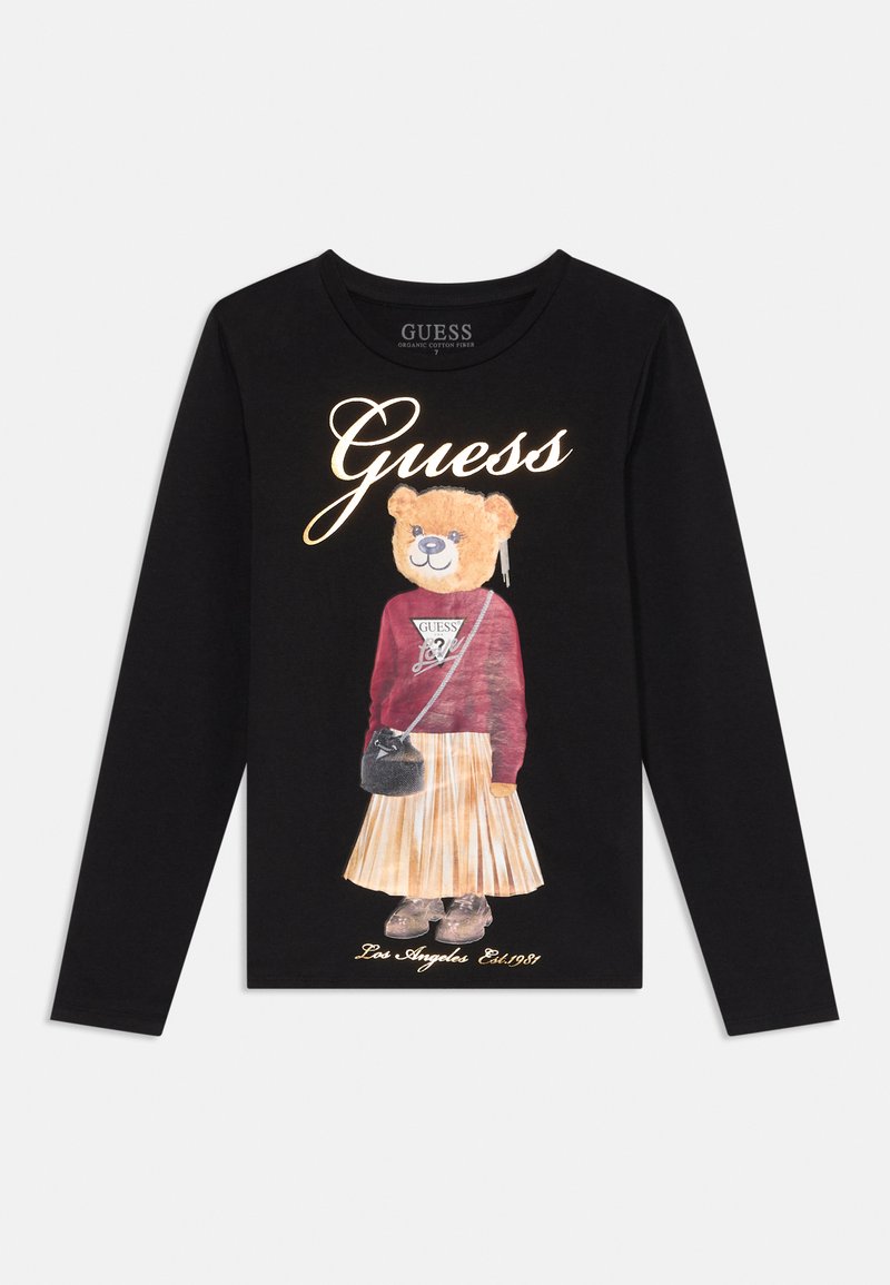 Crna majica dugih rukava s grafikom medvjeda u bordo puloveru i plisiranoj suknji, s oznakom "Guess" i tekstom "Los Angeles Est. 1981".