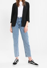 Černé sako, bílé tričko, světle modré džíny s vysokým pasem a černé tenisky s bílými podrážkami. Neformální outfit s vyhrnutými rukávy.