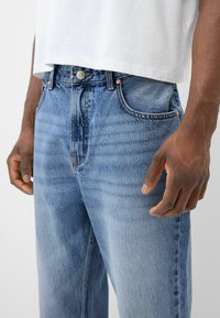 Jeans de mezclilla azul claro de tiro alto, con un estilo clásico de cinco bolsillos y un sutil desvanecimiento. La tela tiene una textura suave.