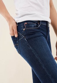 Vaqueros skinny azul oscuro con una textura suave, que cuentan con un bolsillo frontal, detalles de costura en rojo y una sutil etiqueta de logo cerca de la cinturilla.