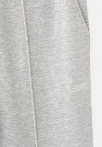 Gray sweatpants made of soft, textured fabric. Features side pockets and an embroidered logo in light gray on the left thigh.