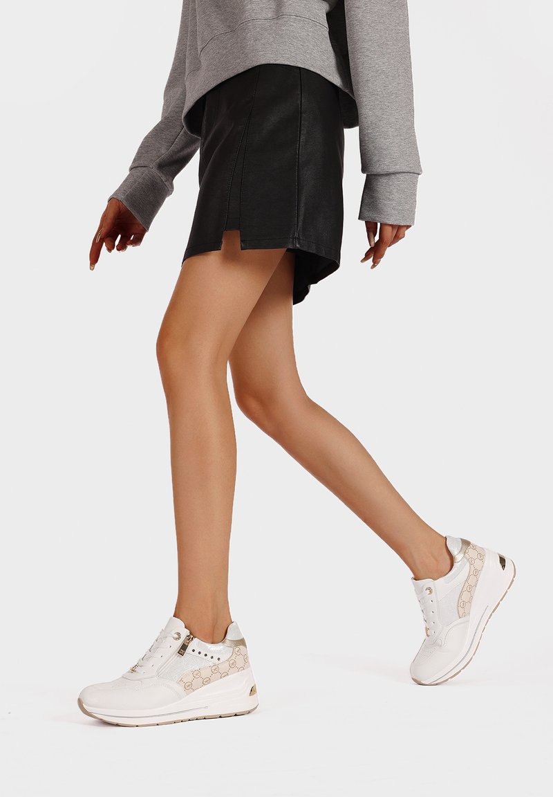 Sneakers bianchi con accenti beige testurizzati, dotati di occhielli e una piccola cerniera. Indossati con una felpa grigia e una gonna in pelle nera.