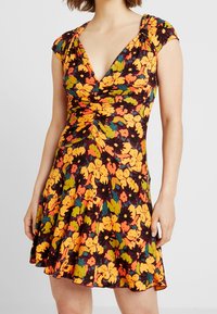 Kwiatowa sukienka z głębokim dekoltem w kształcie litery V, krótkimi rękawami i rozkloszowanym dołem. Czarny tle z intensywnymi pomarańczowymi, żółtymi i zielonymi kwiatami.