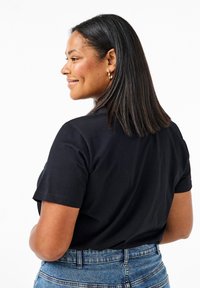 T-shirt nera in cotone con maniche corte, collo a giroclassico, design attillato, indossata con jeans in denim blu a vita alta.