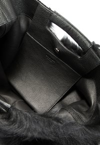 Schwarze Lederhandtasche mit strukturiertem Finish. Innenraum verfügt über eine glatte, flache Tasche. Schwarzer Kunstpelzbesatz akzentuiert die obere Kante.