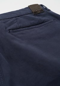 Navy blue trousers featuring a smooth texture, standard pockets, and a leather tag labeled "bugatti" at the waistband.
