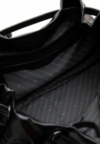 Bolso de mano de cuero negro con una textura suave. El interior cuenta con un forro de tela negra con sutiles rayas diagonales grises y pequeños patrones.