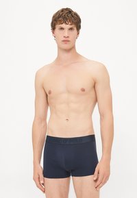 Temno modri boxer kratki hlače, izdelani iz mehke tkanine z gladko teksturo in elastičnim pasom, ki nosi izbočeno logotip.
