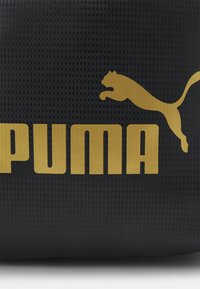 Czarna torba teksturowana z dużym złotym logo "PUMA" i ikoną skaczącego pantery, podkreślająca odważny design i kontrastujące kolory.