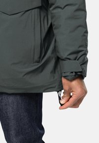 Dunkelgrüne isolierte Jacke mit einer Vordertasche, verstellbaren Bündchen und einem Kordelzugsaum. Glatte Textur und wasserabweisendes Material.