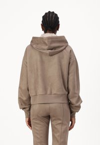 Sudadera corta marrón hecha de tela suave, con capucha, puños acanalados y un ajuste relajado. Combinada con pantalones ajustados a juego.