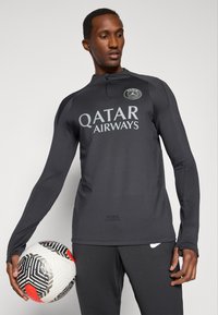 Μαύρη αθλητική μπλούζα με μακρύ μανίκι και ψηλό γιακά. Φέρει τη γραφή "QATAR AIRWAYS" σε μεγάλη λευκή γραμματοσειρά. Συ συνοδεύεται από μια ποδοσφαιρική μπάλα με μαύρο-άσπρο μοτίβο.