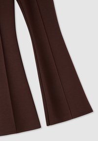 Leggings marroni a zampa con una texture liscia, caratterizzati da pieghe sottili lungo i lati e un tessuto morbido e elasticizzato per il massimo comfort.