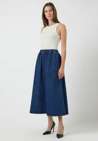 Jupe en denim au design large et longueur cheville, avec une taille élastique. Associée à un haut blanc sans manches près du corps et des talons noirs.