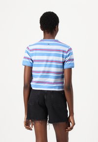 Afgekropte blauwe T-shirt met veelkleurige horizontale strepen (blauw, rood, wit) en korte mouwen, gecombineerd met versleten zwarte denim shorts.