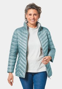 Giacca imbottita azzurro chiaro con colletto alto, motivo a rombi diagonale, zip frontale completa e maniche lunghe, indossata sopra una maglietta bianca.