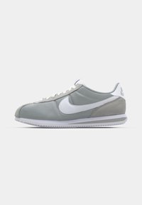 Gray athletic shoe with a suede and textile upper, white Nike swoosh, and white laces. Features a textured rubber sole and padded collar.