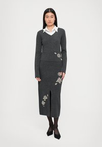 Set format din pulover tricotat gri și fustă tip creion, cu decolteu în V și broderie florală, având o deschidere frontală în fustă și mâneci lungi.