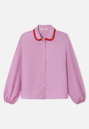 Blouse rose avec un col brodé rouge, manches longues avec poignets élastiques et fermeture boutonnée sur le devant. Tissu lisse, coupe décontractée.