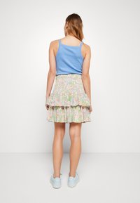 Débardeur bleu clair associé à une jupe florale à plusieurs niveaux ; présente des couleurs pastel et un ourlet à volants ; porté avec des baskets bleu clair.