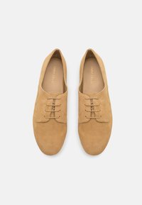 Pantofi din suede de culoare maron deschis, cu un design clasic cu șireturi, vârf rotunjit și textură netedă; prezintă detalii subtile de cusătură pe laterale.